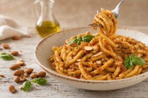 Skål med kogt busiata vendt i mandel- og tomatpesto, en gaffel løfter en snoning op