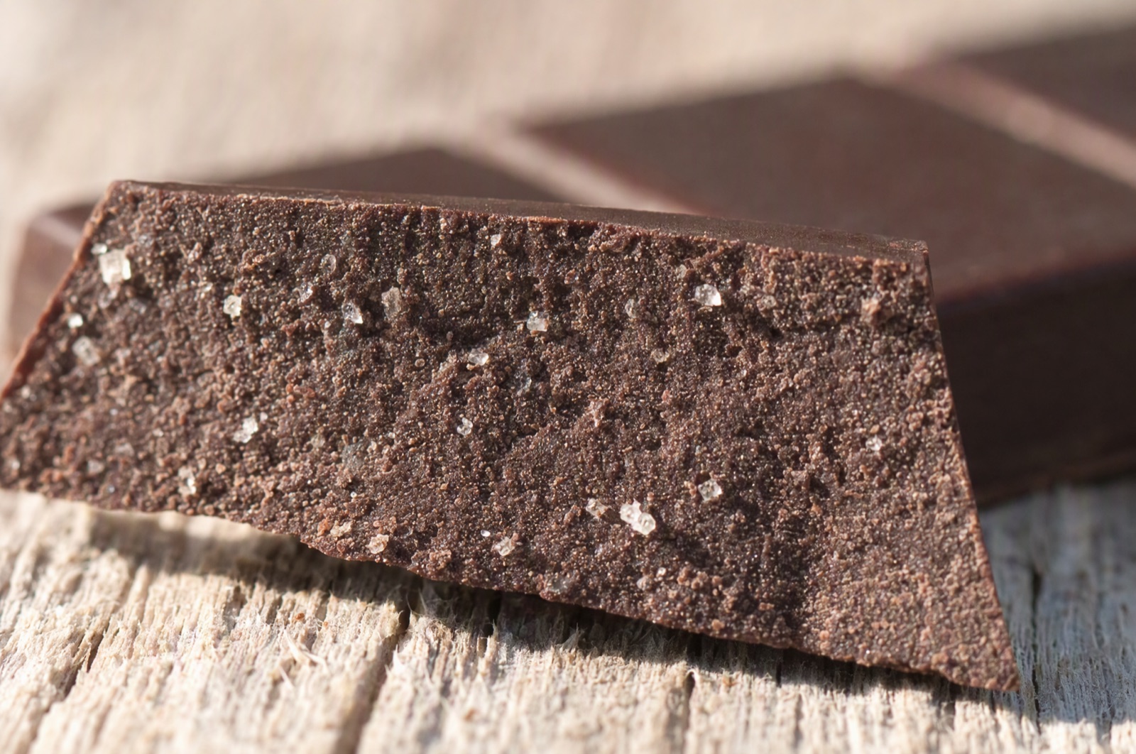 Nærbillede af en brækket mørk chokoladebar med mat, kornet brudflade og synlige sukkerkrystaller