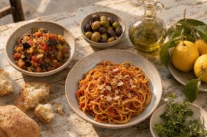 Siciliansk bord set oppefra med pasta i tomat og mandel, caponata, oliven, brød, olivenolie og citroner