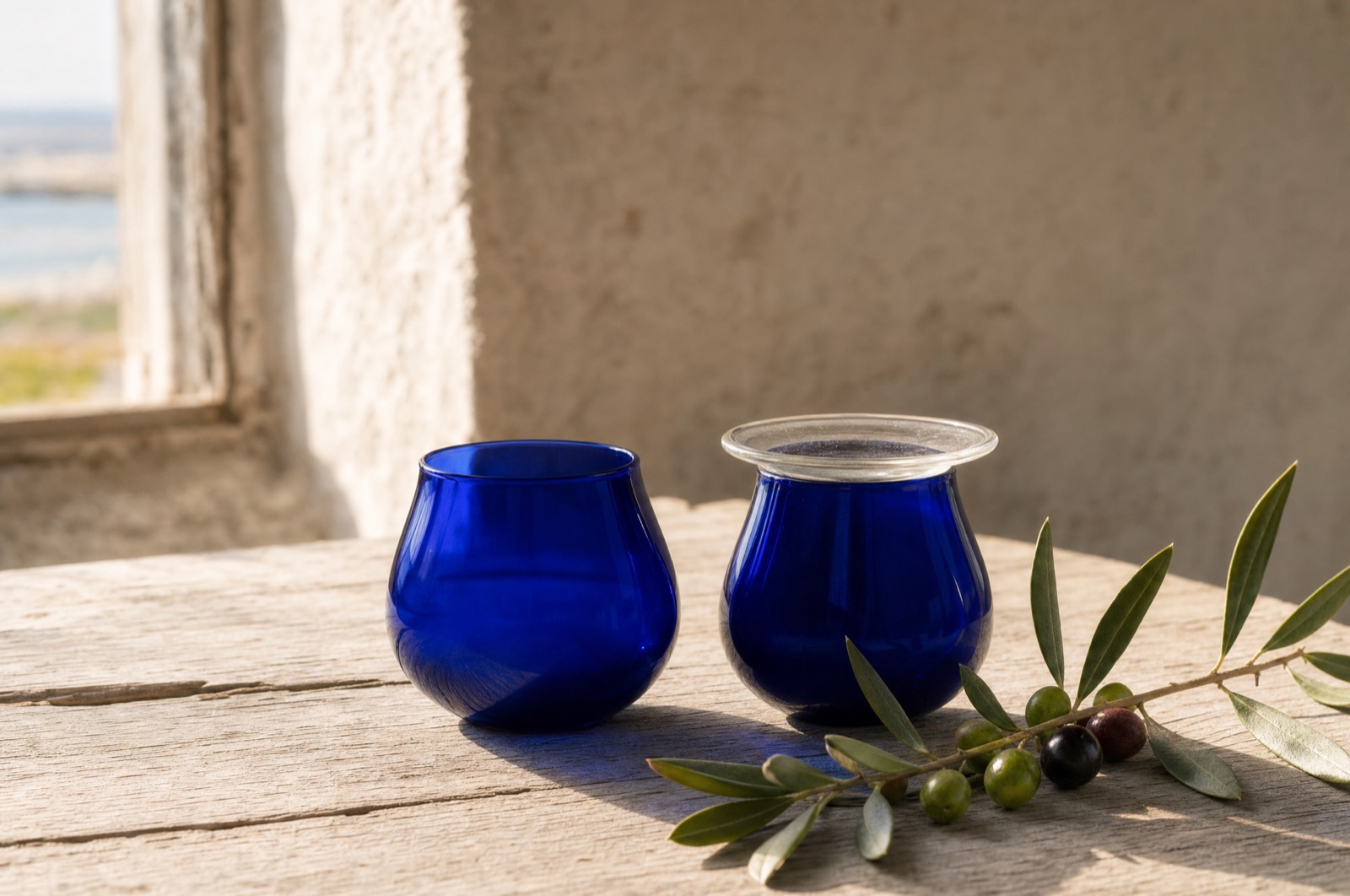 To glas olivenolie ved siden af hinanden på et bord, det ene dybgrønt og det andet lyst gyldent
