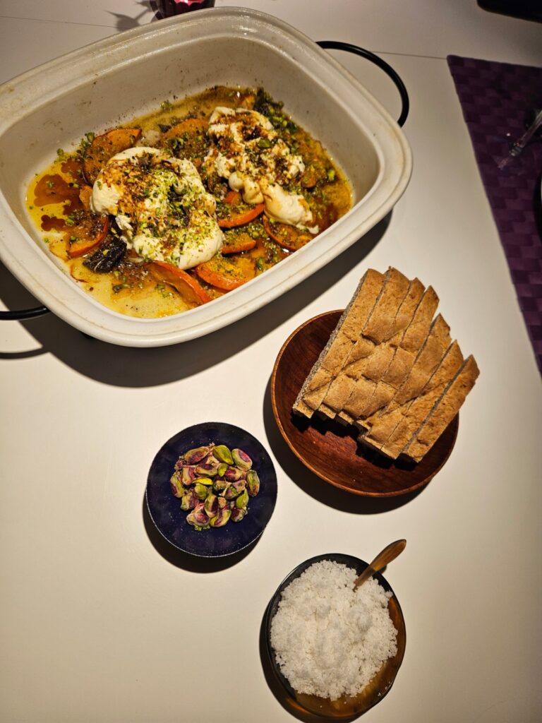 Bagt hokkaido med burrata, pistacier og salviesmør i et ovnfast fad, med brød og havsalt ved siden af